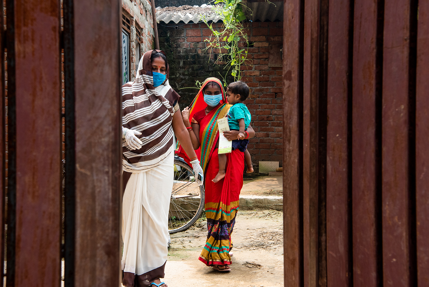©Gates Archive/Saumya Khandelwal. Caption: L-R Neelam Kumari,  accredited social health activist (ASHA), accompanies a mother, Uma and her child, Bhawna, to the primary school for a Village Health Sanitation and Nutrition Day Session in Sandauli, Uttar Pradesh, India on September 16, 2020. ASHAs have been instrumental in spreading awareness about COVID-19  and facilitating health services at the rural level.