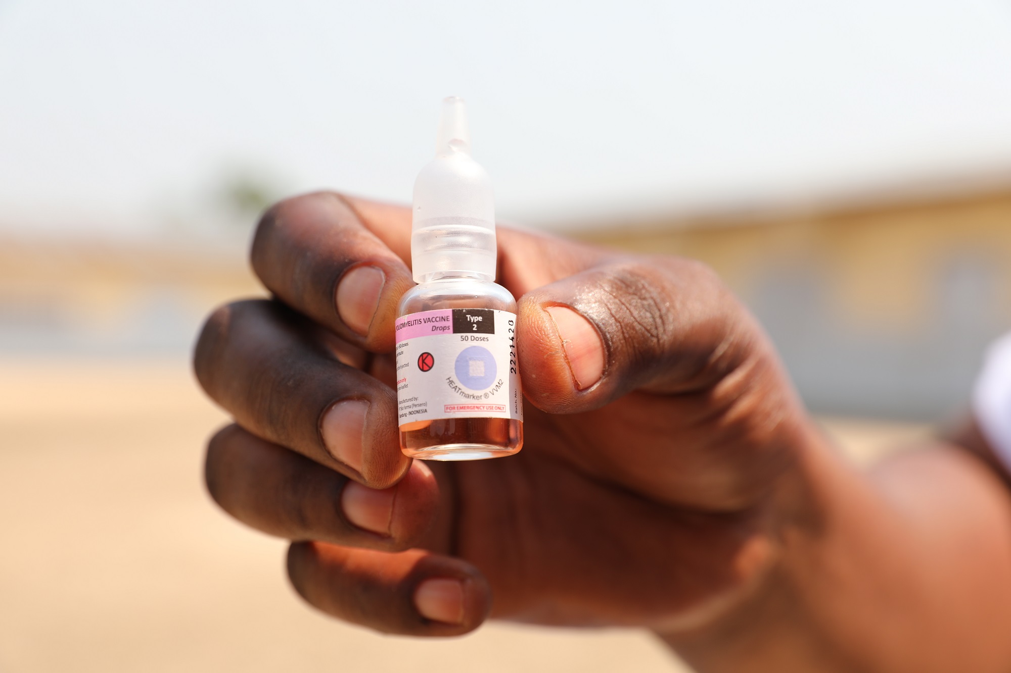 A hand holding a small bottle of vaccine