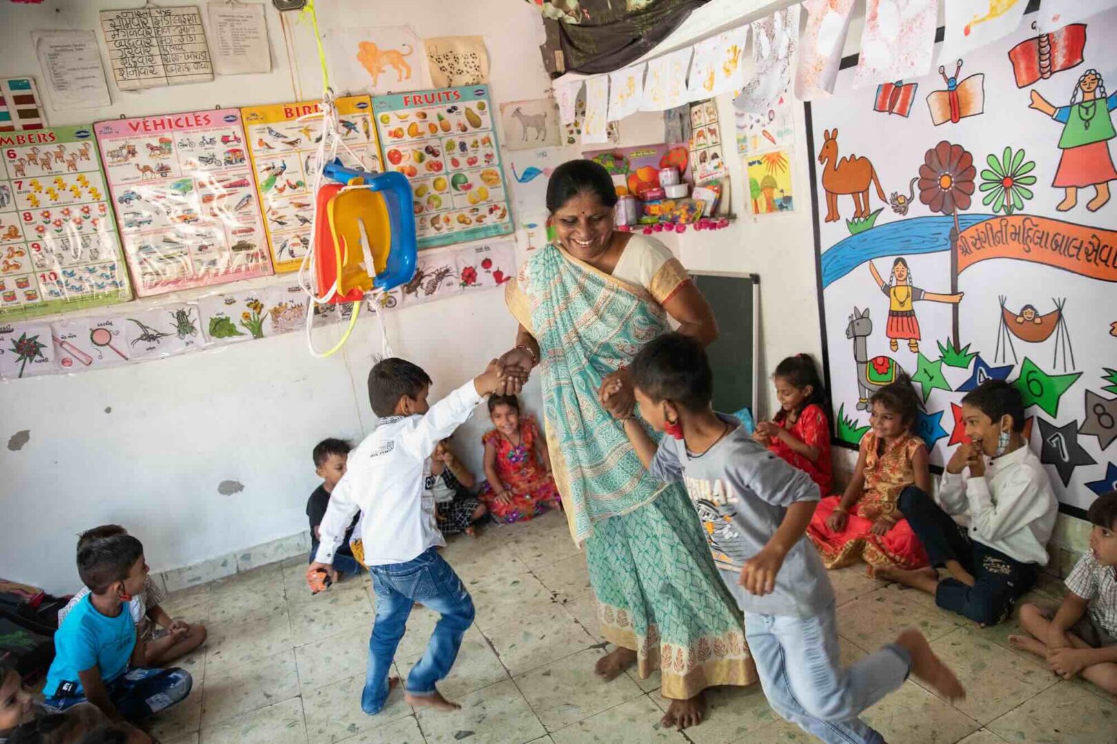 A woman named Jashodaben plays with children at a SEWA (Self-Employed Women's Association) childcare center in Ahmedabad, Gujarat, India. This childcare facility enables local women to work while their children receive care.