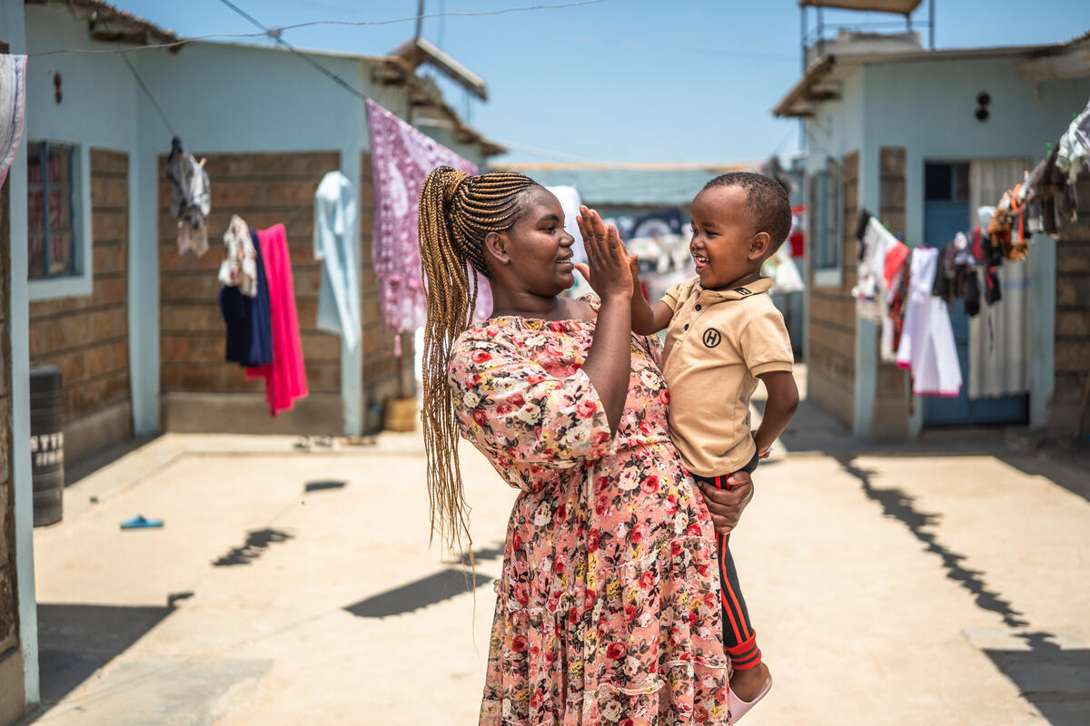 Christine and her son smiling and high-fiving at their home in Wote, Makueni County, Kenya